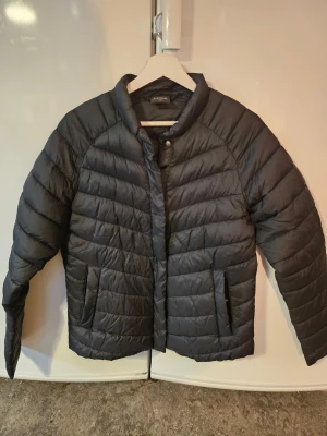 Svart jacka från Everest - Säljer en svart jacka från Everest med snygg quiltad design och hög krage. Jackan har två fickor med dragkedja och stängs med både dragkedja och tryckknappar. 