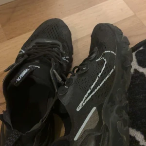Nike react  - Säljer ett par svarta sneakers från JX VSN med vit detalj på sidan och grov sula. Skorna har snörning och meshpaneler för extra ventilation. Perfekta för dig som vill ha en sportig och stilren look.