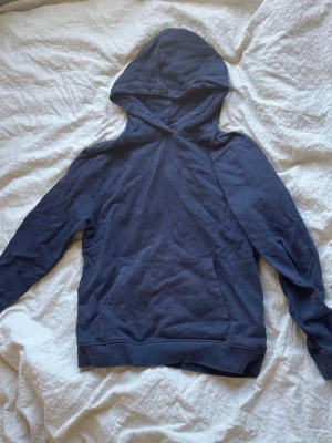 Mörkblå hoodie med magficka - En enkel och stilren mörkblå hoodie med huva och stor magficka framtill. Hoodien har långa ärmar och ribbade muddar vid ärmslut och nederkant. Perfekt för en avslappnad och chill look.