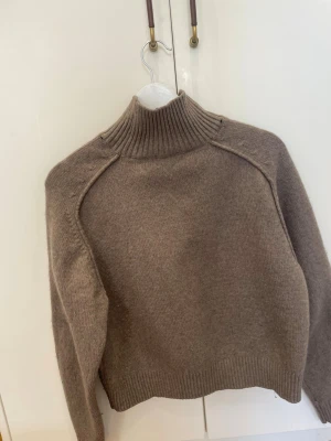Beige stickad polotröja - Mysig beige stickad polotröja med hög ribbad krage och långa ärmar. Tröjan har en rak, något boxig passform och ribbade muddar vid ärmslut och nederkant. Perfekt för kalla dagar och enkel att matcha med olika outfits.