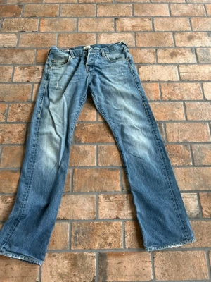 Blå bootcut jeans från true religion - Säljer ett par klassiska blå bootcut jeans från true religion med slitningar och ljusare partier framtill. Jeansen har fem fickor, normal midja. Perfekta för en avslappnad och trendig look.
