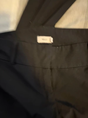 Svarta kostymbyxor från Nelly - Säljer ett par klassiska svarta kostymbyxor från Nelly. Byxorna har raka ben, hällor för skärp och en stilren design. Perfekta för dig som vill ha en clean och enkel look. Materialet känns mjukt och följsamt.