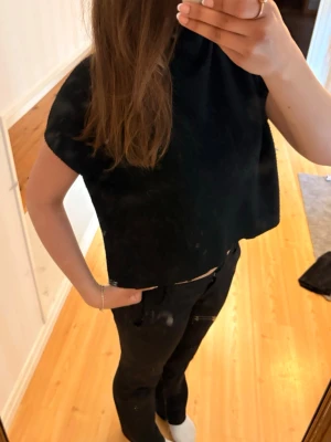 Svart polo topp - En enkel svart polo topp med boxig passform och korta ärmar. Perfekt att styla med höga jeans eller kjol för en avslappnad look. Toppen är ärmlös och har en minimalistisk design utan synliga detaljer.