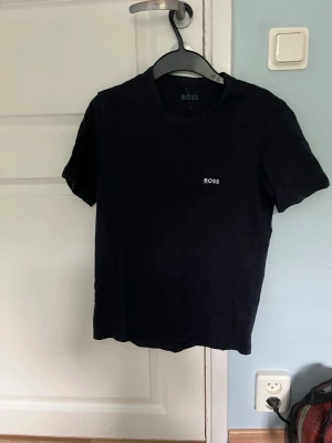 Svart t-shirt från BOSS - Klassisk svart t-shirt från BOSS med rund halsringning och diskret logga på bröstet. Enkel och stilren design som passar till det mesta. Tillverkad i mjukt material för skön känsla hela dagen.
