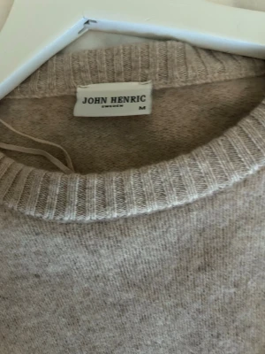 Beige stickad tröja John Henric - Säljer en beige stickad tröja från John Henric i storlek M som har krympt till storlek S. Tröjan har rund halsringning och ribbade muddar vid ärmslut och nederkant. Materialet ser mjukt och lite luddigt ut, perfekt för kyligare dagar.