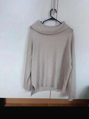 Beige stickad polotröja - Mysig beige stickad polotröja med bred krage och långa ärmar. Tröjan har ribbade muddar vid ärmslut och nederkant samt en avslappnad passform. Perfekt för kalla dagar och enkel att matcha med jeans eller kjol.