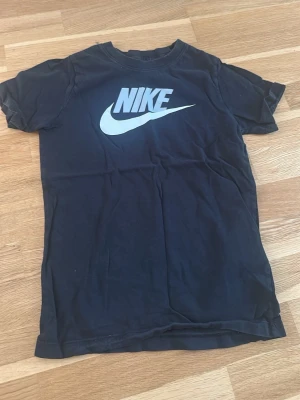 Svart Nike t-shirt med logga - Snygg svart t-shirt från Nike med stor vit logga och swoosh på bröstet. Klassisk rund halsringning och korta ärmar. Perfekt till vardags för en sportig och avslappnad stil.