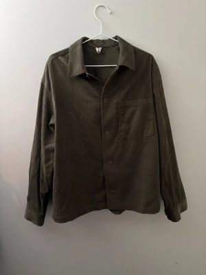 Arket overshirt i manchester - Säljer en stilren olivgrön overshirt i mjuk manchester med klassisk krage, knappstängning och en bröstficka. Perfekt lager på lager-plagg med avslappnad passform och långa ärmar. Enkel och clean design som passar till det mesta.