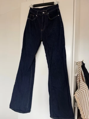 Mörkblå bootcut jeans - Säljer ett par mörkblå bootcut jeans med hög midja och kontrastsömmar. Klassisk femficksmodell och knappgylf. Perfekta för dig som gillar en retroinspirerad look och vill ha ett par jeans med lite vidare ben.