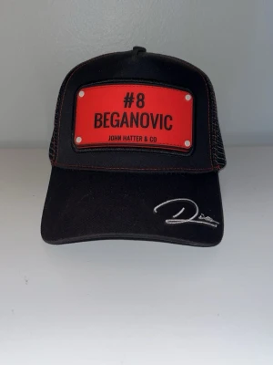 Svart keps John Hatter & Co Beganovic - Svart keps med röd skylt framtill med texten '#8 Beganovic' och broderad signatur på skärmen. Kepsen har mesh baktill och justerbar rem. Nypris 495kr. Snygg keppa för dem som är F1 intresserade 😇