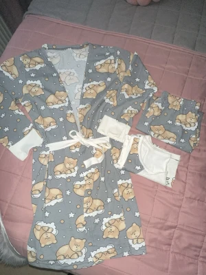 Grå pyjamas ( 3delar) oanvänd - Supersöt grå morgonrock med gulligt björnmönster, vita muddar och knytband i midjan. Mjuk bomullskänsla och långa ärmar. Perfekt för mysiga hemmakvällar eller lata morgnar. Matchande pyjamasbyxor och tröja ingår.