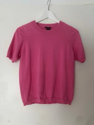 Rosa topp  - Snygg rosa stickad topp från Lindex med rund halsringning och korta ärmar. Mjuk och bekväm kvalitet med ribbade kanter vid ärmslut och nederkant.
