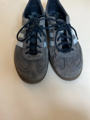 Adidas Spezial gråblå sneakers - Säljer ett par Adidas Spezial sneakers i grå mocka med ljusblå ränder och mörkblå snören. Skorna har klassisk låg profil och gummisula. Perfekta för dig som gillar retrostil och streetwear. Andvänd typ 1 gång.