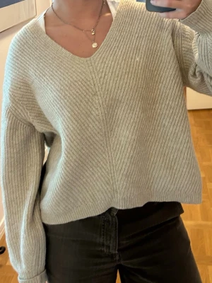 Beige stickad tröja med v-ringning - Mysig beige stickad tröja med djup v-ringning och avslappnad passform. Tröjan har långa ärmar och ribbstickad struktur som ger en trendig look. Perfekt att matcha med jeans eller kjol för en enkel och snygg outfit. Storlek M men passar S