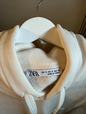 Vit hoodie från Zara med ficka - Klassisk vit hoodie från Zara med stor känguruficka framtill och justerbar dragsko i huvan. Tillverkad i mjukt material med borstad insida för extra komfort. Perfekt oversized look och enkel att matcha med allt.