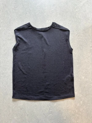 Mörkgrå ärmlös topp - En stilren mörkgrå ärmlös topp med rund halsringning. Perfekt att matcha med jeans eller kjol för en enkel och clean look eller festival vibes. Storlek XS men sitter som M. 