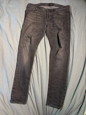 Grå slim fit jeans från j.lindeberg - Snygga grå slim fit jeans från J.lindeberg med klassisk femficksdesign och dragkedjegylf. Jeansen har en lätt tvättad look och smal passform som sitter tajt längs benen. Perfekta för en trendig och avslappnad stil.