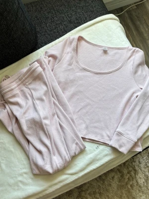 Ljusrosa ribbat loungewear-set - Mysigt loungewear-set från Gilly Hicks i ljusrosa ribbat material. Setet består av en långärmad topp med bred, rundad urringning och matchande byxor med resår i midjan. Perfekt för chill dagar hemma. Materialet är mjukt och stretchigt för extra komfort.🌸 nypris: ca 800kr