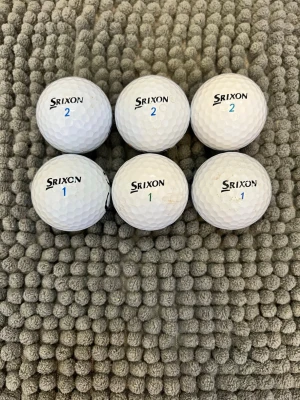 Srixon   golfbollar - Sex vita golfbollar från Srixon och Warbird. Bollarna har texten 'SOFT FEELING', 'WARBIRD' och 'AD333' samt siffror i blått och svart. Klassisk rund form och tillverkade i slitstarkt material, perfekta för golfbanan.