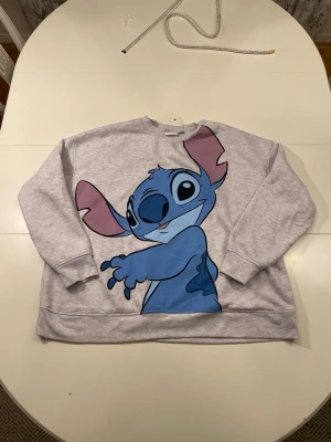Grå sweatshirt med Stitch-motiv - Grå sweatshirt med ett stort tryck av Disney figuren Stitch på framsidan.   Storlek: XL Längd: 62 cm Armhålsbredd: 67 cm   Ställ gärna frågor! :)