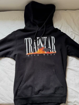 Trapstar London hoodie svart - Svart Trapstar hoodie med Wild West print framtill. Bra skick utan större defekter. Tjock och skön kvalitet. Köpt för några år sedan från trapstars egna sida men sparsamt använd.