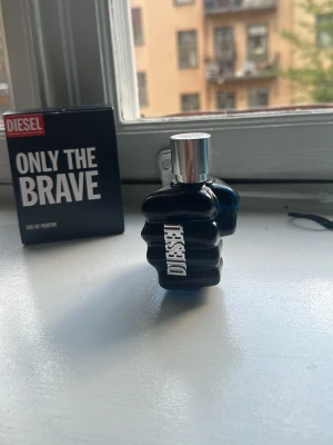Diesel Only The Brave parfym - Diesel Only The Brave Eau de Parfum med en unik flaska formad som en knytnäve i mörkblått glas och silverfärgad kork. Märkets logga syns tydligt på flaskan. En cool och modern doft som sticker ut i badrumshyllan. Trots att flaskan är använd så finns det ungefär 85% kvar. Nypris 785kr. 50ml.