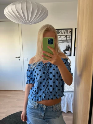 Blå prickig sommartopp - Snygg blå topp med svarta prickar och knytning framtill💙Toppen har korta ärmar med resår och knappar längs hela framsidan. Går att ha både off-shoulder och med ärmarna uppe. Perfekt till sommaren!