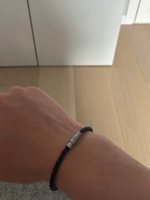 Svart armband från Boss - Snyggt svart flätat armband från BOSS med ett stilrent magnetlås i silverfärgad metall. Perfekt accessoar för dig som gillar en enkel men trendig look. Armbandet har en diskret logga ingraverad på låset och passar till många olika stilar.