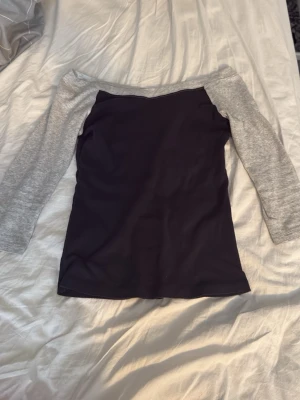 Svart topp med grå ärmar - Snygg off shoulder topp i svart med kontrasterande grå ärmar. Modellen har trekvartsärm och en bred halsringning som sitter snyggt över axlarna. Perfekt till jeans eller kjol för en trendig look. Från brandy Melville, onesize. Knappt använd
