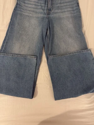 Blåa wide leg jeans - Säljer ett par ljusblå jeans med extremt vida ben och hög midja. Jeansen har klassisk femficksdesign och är tillverkade i denim. Perfekta för dig som gillar en trendig och avslappnad stil med mycket attityd.