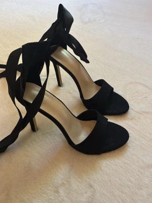 Svarta höga pumps med knytband - Stilrena svarta pumps med öppen tå och höga klackar. Skorna har breda band över tårna och långa knytband runt ankeln för en trendig look. 