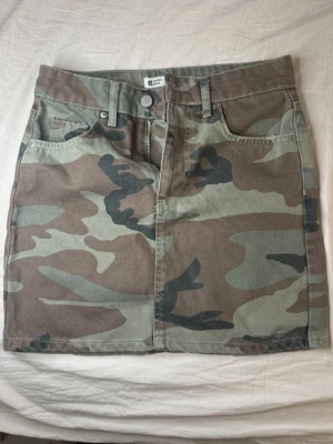Kjol med fickor - Snygg minikjol i camouflage-mönster med klassiska jeansfickor fram och bak samt bälteshällor. Kjolen har en rak passform men formar kroppen fint. Perfekt nu inför sommaren.