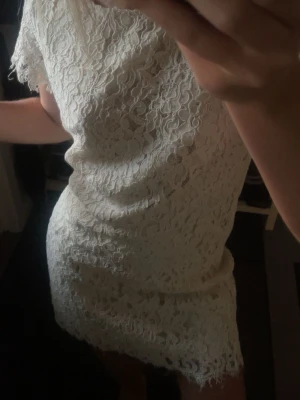 Vit spetsklänning med kort ärm - Söt vit kortklänning i spets med korta ärmar och rund halsringning. Klänningen har ett feminint blommigt spetsmönster och är fodrad undertill. Perfekt för sommarens alla tillfällen och ger en romantisk vibe.