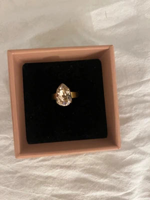 Guldfärgad ring med droppformad sten - Snygg guldfärgad ring med en stor, droppformad klar sten som fångar ljuset. Ringen har en enkel men elegant design och passar perfekt för dig som gillar statement-smycken. guld färgen har gått bort lite på vissa ställen men fortfarande jättefin 