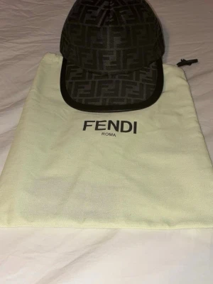 Fendi keps med FF-mönster - Snygg keps från Fendi med klassiskt FF-monogram i svart och mörkgrått. Kepsen har böjd skärm, justerbar rem bak och är tillverkad i ett tygmaterial. Perfekt accessoar för att lyfta din streetwear-look.