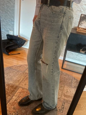 Hope Distressed Rush Jeans relaxed bootcut - Säljer ett par grå raka jeans med slitning och hål på ena knät. Jeansen har hög midja, fem fickor och klassisk denimlook. Perfekta för en avslappnad och trendig stil. Materialet är kraftig bomullsdenim.