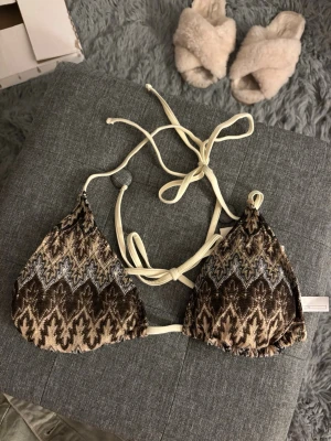 Mönstrad bikiniöverdel från BeckSöndergaard - Snygg trekantsbikini från BeckSöndergaard med beige och brunt mönster, justerbara knytband i nacken och ryggen. Materialet är mjukt och stretchigt, perfekt för sommardagar på stranden. Färgen är MOCHA BROWN