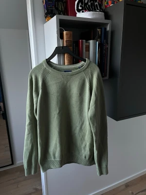 Grön stickad tröja från Gant - Snygg ljusgrön stickad tröja från Gant med rund halsringning och diskret broderad logga på bröstet. Tröjan har ribbade muddar vid ärmslut och nederkant samt ett stilrent mönster vid axlarna. Perfekt för lager-på-lager-stil.