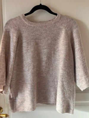 Beige oversized stickad tröja - Mysig beige stickad tröja med avslappnad passform och trekvartsärmar. Tröjan har rund halsringning och ribbade muddar vid ärmslut och nederkant. Perfekt för lager på lager och en chill look.