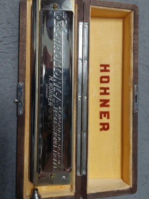 Hohner kromatisk munspel i etui - Kromatisk munspel från Hohner, modell Chromonica 64, i original trälåda med gul vadderad insida och röd logotyp. Munspelet är i metall med ingraverad text och har en klassisk silverfärgad finish. Perfekt för dig som vill spela musik med stil.