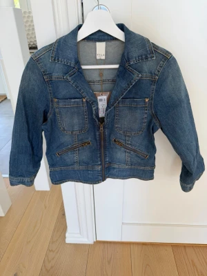 VILA jeansjacka med dragkedja – ny med tags kvar - Säljer en superfin och trendig kort jeansjacka från danska märket Vila. Jackan har en modern figursydd passform och skiljer sig från klassiska jeansjackor genom sin robusta dragkedja framtill istället för knappar, vilket ger ett snyggt och lite tuffare uttryck.  Detaljer: • Kort och figursydd modell • Två stora bröstfickor med lock • Två sidofickor med synliga dragkedjor • Stilren och lättmatchad design • Helt ny och oanvänd • Original prislapp sitter kvar  Nypris: 599,95 kr  