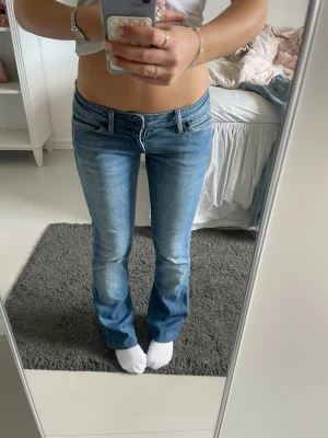 blå bootcut jeans från wrangler - Säljer ett par ljusblå bootcut jeans från wrangler med klassisk femficksdesign. Jeansen har låg midja och subtila detaljer på bakfickorna. Perfekta för dig som gillar en avslappnad och trendig look.