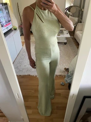 Mintgrön glittrig jumpsuit - Snygg mintgrön jumpsuit med glittrigt tyg och halterneck. Smal passform upptill och utsvängda ben. Cool cut-out detalj vid halsen. 