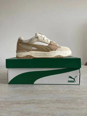 Puma sneakers - Stilrena sneakers från Puma i beige och ljusbruna toner med vit sula. Skorna har en klassisk låg siluett, ovandel i mocka och mesh samt vita skosnören. Perfekta för dig som gillar en clean och trendig look.
