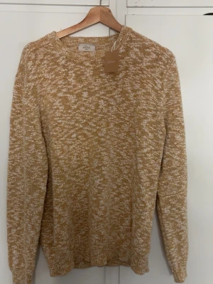 Sprillans ny tröja Altea Milano - Stickad tröja från Altea Milano i beige och vitt melerat garn. Tröjan har rund halsringning, långa ärmar och ribbade muddar vid ärmslut och nederkant. Perfekt för lager på lager och ger en avslappnad men snygg look.