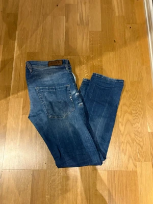 Blå raka jeans med slitningar - Snygga blå jeans med raka ben och diskreta slitningar framtill. Klassisk femficksmodell med knappgylf och läderpatch bak i midjan. Jeansen har en tvättad look och är tillverkade i denim, perfekt för en avslappnad stil.
