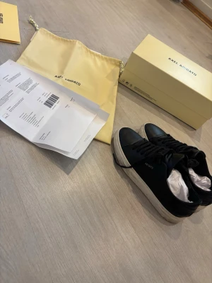 Svarta Axel Arigato sneakers i läder - Snygga svarta sneakers från Axel Arigato med ovandel i läder och vit, chunky sula. Klassisk låg modell med svarta skosnören och diskret guldfärgad logga på sidan. Kommer med originalkartong och dustbag. Kvinno finns!! 