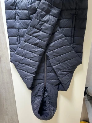 Svart pufferjacka med huva - Snygg svart pufferjacka med huva och dragkedja framtill. Jackan har två sidofickor med dragkedja och quiltad design med horisontella sömmar. Perfekt för kalla dagar när du vill hålla dig varm och stilren.