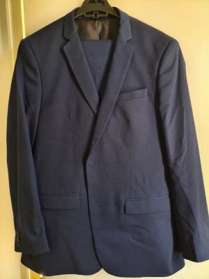 Mörkblå kavaj från Zara Man - Säljer en stilren kostym från Zara Man i mycket fint skick. En tidlös marinblå kostym med slim fit-passform — perfekt för bröllop, middagar, kontor eller en mer uppklädd vardagsstil. Detaljer: Märke: Zara Man Passform: Slim Fit Färg: Marinblå – en klassisk och elegant mörkblå nyans Skick: Mycket fint skick Tillverkad i: Marocko Kavaj: Storlek: EU 54 Byxor: Storlek: EU 46 / US 36 Design: Skräddad slim fit-modell med en modern och stilren silhuett som fungerar lika bra uppklädd som mer avslappnat.