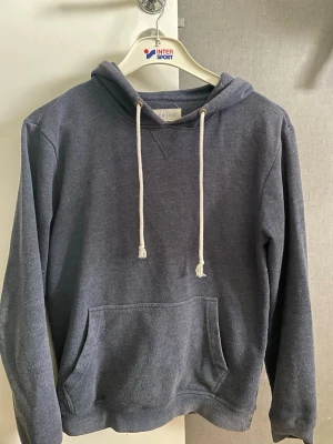 Mörkblå hoodie från Pier One - Mysig mörkblå hoodie från Pier One med klassisk känguruficka och vita dragsnören i huvan. Perfekt för en avslappnad stil. Tillverkad i mjukt material som känns skönt mot huden. Långärmad och enkel att matcha med jeans eller joggers.